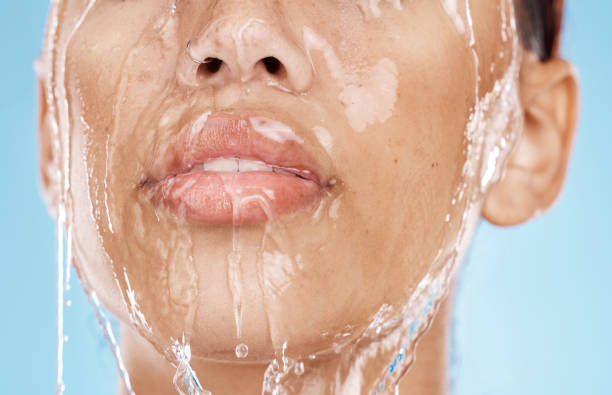 Woman, washing face or water drops skincare on blue background studio in lips healthcare wellness, hygiene cleaning or mouth moisture grooming. Zoom, beauty model or facial water splash in wet shower mujer, lavado de cara o gotas de agua cuidado de la piel sobre fondo azul estudio en labios cuidado de la salud bienestar, limpieza de higiene o aseo de la humedad de la boca. zoom, modelo de belleza o salpicadura de agua facial en ducha húmeda
