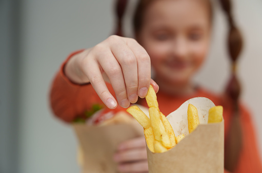 Close-up photo of cheerful white girl taking fries from a box, focus on hand