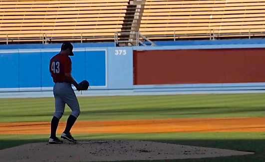 A baseball pitcher is on the mound getting ready for his next pitch. The pitcher and the field are in shadows and create a sense of solitude.