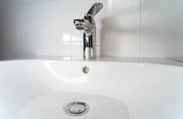 A stream of clean water flows from the mixer into the kitchen sink. Selective focus.