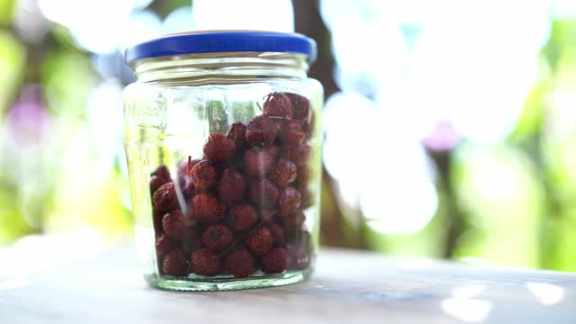 Dried rose hips in a glass jar with a lid stand on a table on the balcony
