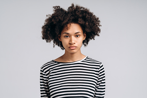 Serious multiracial curly brunette woman looking at camera with sad expression. People emotions concept. Studio shot, isolated on while background