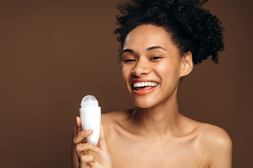 Outgoing multiracial woman preparing to applying antiperspirant on her body. Naked shoulders woman smiling toothy