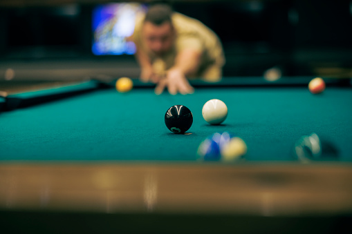 At a billiard bar, a player prepares for a shot to sink the ball.
