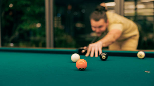 ein spieler stellt einen schuss auf, um den ball in einer billardstange zu versenken. - setting the table sports clothing practicing success stock-fotos und bilder