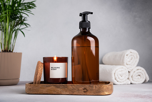 Eco friendly bathroom concept. Brown dispenser bottle of shower gel and candle for relax and spa on wooden tray on grey concrete background