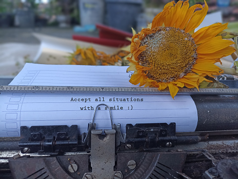 Life inspirational motivational quote - Accept all situations with a smile. With typewriting text on white line paper on an old retro typewriter and wilted sunflower vintage. Acceptance concept.