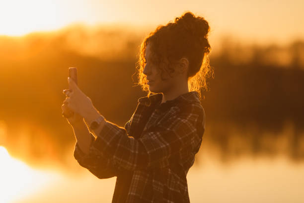 istock Curly woman with mobile phone on sunset background. 1472848352