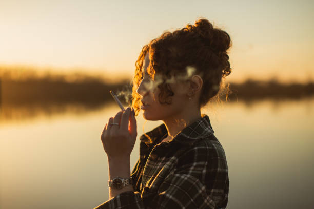 Curly woman smoking cigarette on sunset background. Silhouette stock photo