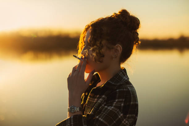 mulher encaracolada que fuma cigarro no fundo do pôr do sol. silhueta - nicotine healthcare and medicine smoking issues lifestyles - fotografias e filmes do acervo