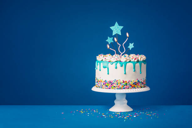 濃い青の背景に白い誕生日のドリップケーキとティールガナッシュ、スタートッパー、楽しいキャンドル