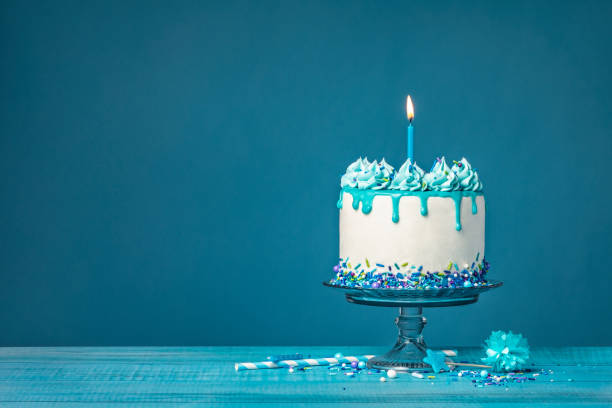 istock White birthday drip cake with teal ganache and lit candle over blue background 1472849611