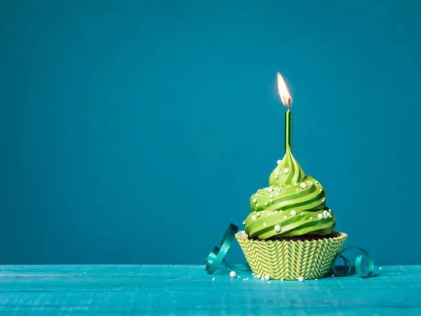 Photo of Green cupcake with lit candle on a blue background.