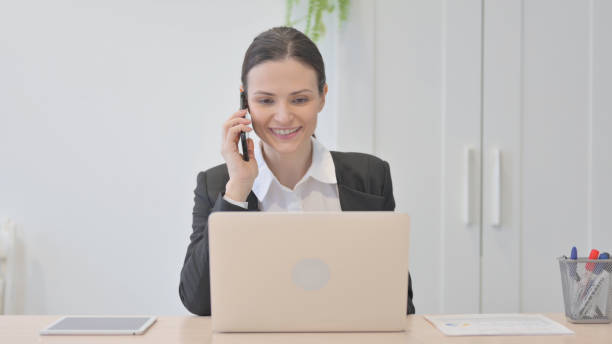 joven empresaria hablando por teléfono mientras usa la computadora portátil - 13427 fotografías e imágenes de stock