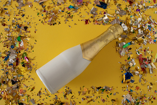 A glass bottle full of champagne on a yellow table full of colorful confetti