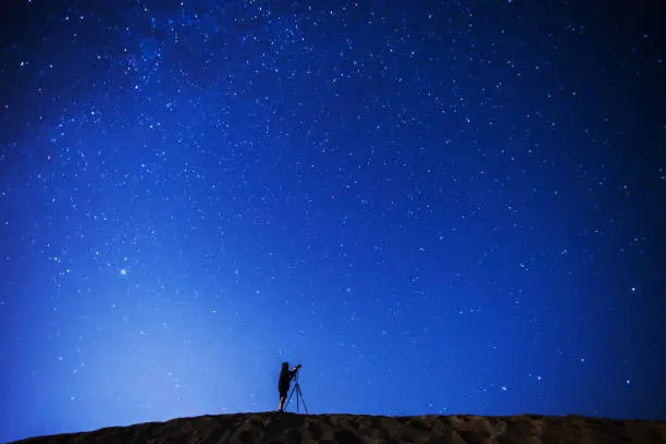 Photo of Photographer taking pictures of the night sky. Silhouette of man against background of night starry sky. Stars