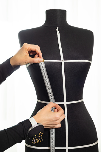a dressmaker takes measurements from a female mannequin. isolated. tailoring is handmade.