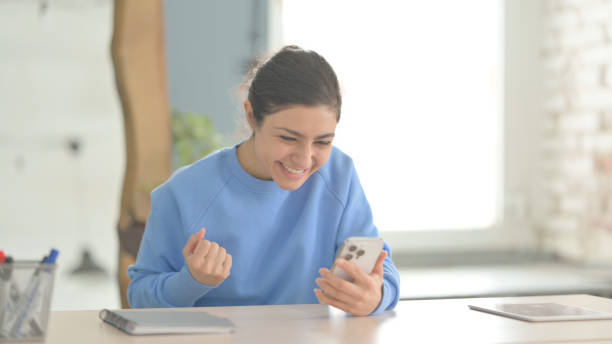 istock Successful Indian Woman Celebrating Win on Smartphone 1472860627