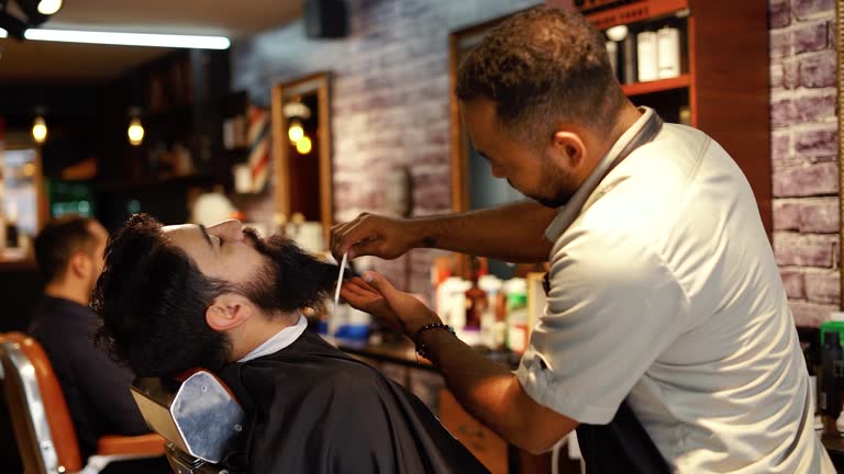 Barber grooming a customer's beard.