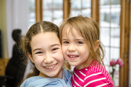 Headshot of two young girls toothy smiling at camera while hugging