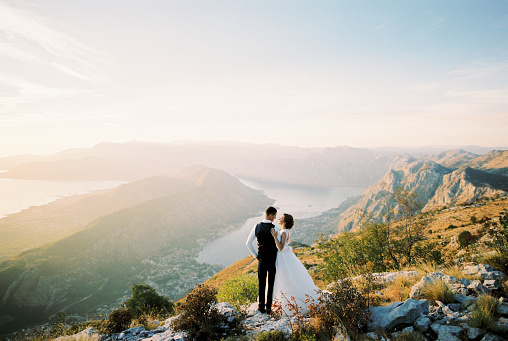 Groom hugs bride on a mountain above the Bay of Kotor. High quality photo
