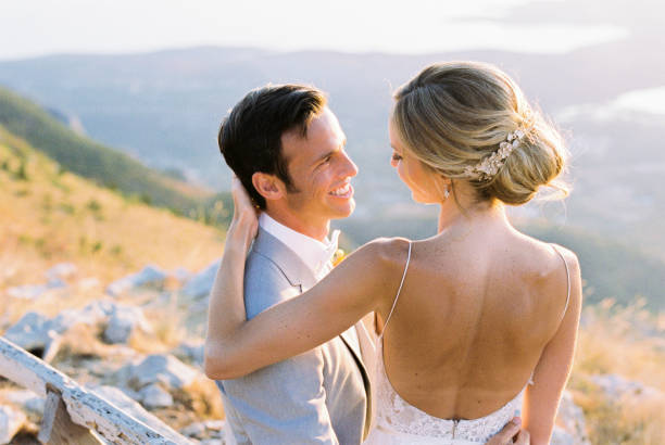 Bride sits on the lap of groom, hugging his shoulders. High quality photo