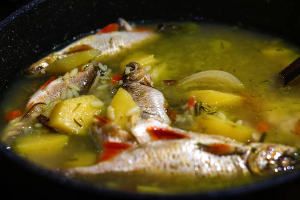 Defocus fish Soup Ukha. Perch fish in a clear broth with diced root vegetable served in white plate on wooden table. Selective focus. Fresh fish soup in pan. Out of focus.