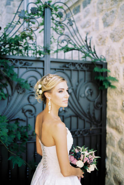 istock Bride with a bouquet stands sideways near a stone house 1472874981