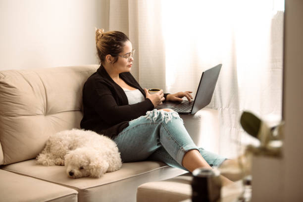 istock Young woman drinking coffee while using her laptop to work from home 1472877621