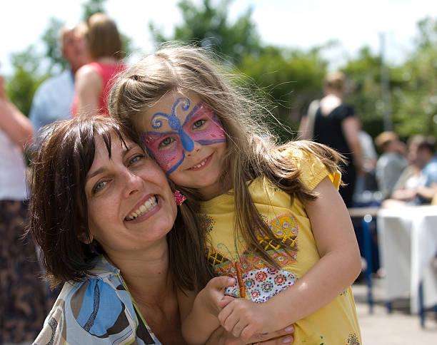 Mother and daughter with face paint cuddle Mother and Face Painted Daughter cuddle at summer fair face paint stock pictures, royalty-free photos & images