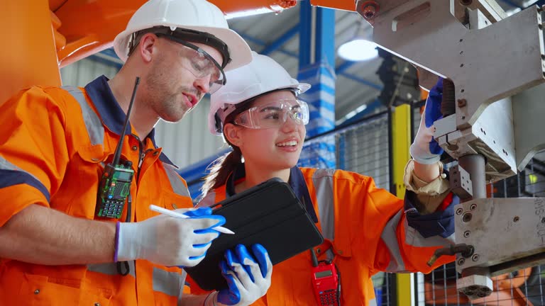 Engineer man and woman talking and discussion about robot arms technology intelligence and innovation while looking digital tablet at factory, people meeting and check machine robot, industry concept.