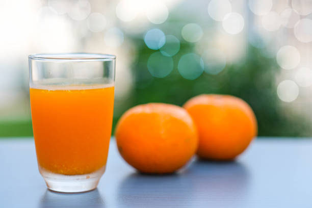 Fresh oranges juice and there are two oranges behind ,place on dark blue table with blur nature background and bokeh
