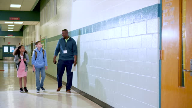 Teacher walks with elementary students in school hallway