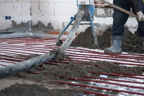 istock Semi-dry floor screed - a worker shovels a construction mixture through a special sleeve for cementing and leveling on underfloor heating pipes. 1472898892