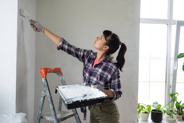 kobieta w wałku malarskim i białej farbie maluje ścianę domu na drabinie. prace budowlane i kosmetyczne w domu, malowanie ścian, barwienie, prace wykończeniowe własnymi rękami - paint brushing house painter wall zdjęcia i obrazy z banku zdjęć
