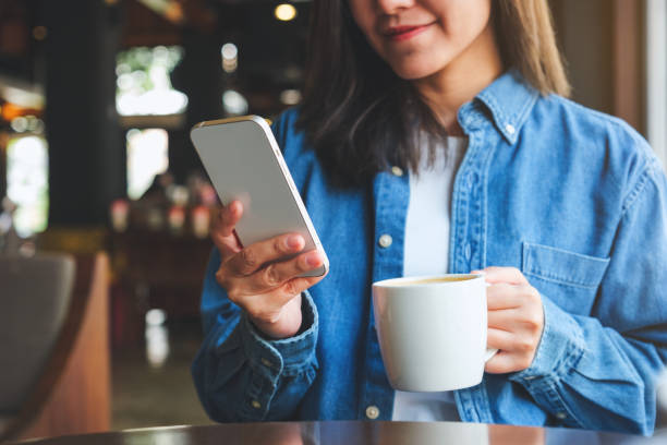 istock Closeup image of a young woman holding and using mobile phone while drinking coffee in cafe 1472907599