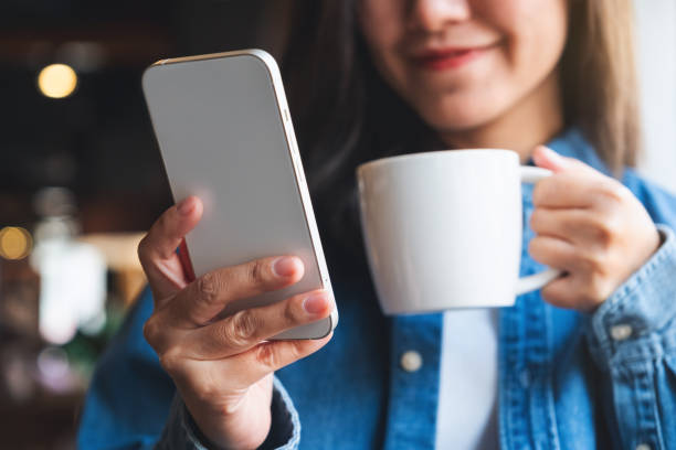 istock Closeup image of a young woman holding and using mobile phone while drinking coffee in cafe 1472907603