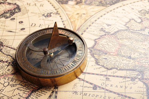 Magnetic compass with sundial on a vintage world map. Travel, geography, navigation concept.