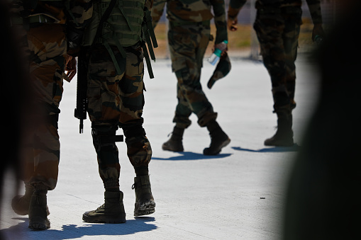 Boots and guns of Indian Army on guard and walking on tarmac.