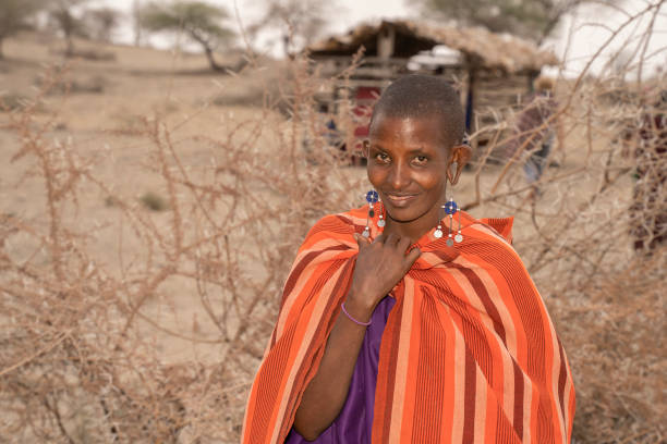 Karatu, Tanzania - October 16th, 2022: A portrait of a masai woman in traditional clothes and jewelry, by her village's thorn fence.