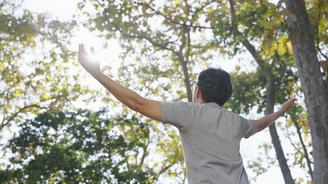 Slow Motion of Arms Outstretched Asian Man Standing in the Forest and Looking at The Sun