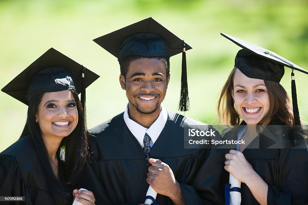 Multi-Racial Classmates Smiling On Graduation Day Two female and one male with big smiles wearing cap and gown on graduation day. Graduation Stock Photo