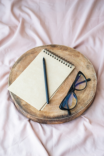 Spiral notebook, pen and eyeglasses on wooden tray. Planning concept. Stationary still life on bed.
