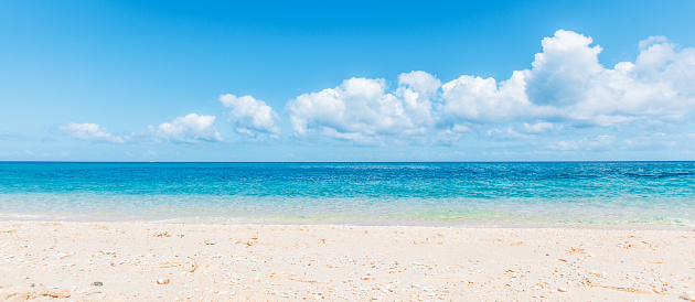 Lone striped umbrella leaning into wind on a sandy French beach in summer with a blue clear sky background