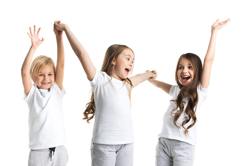 Happy smiling three children in white clothes holding raised hands isolated on white background