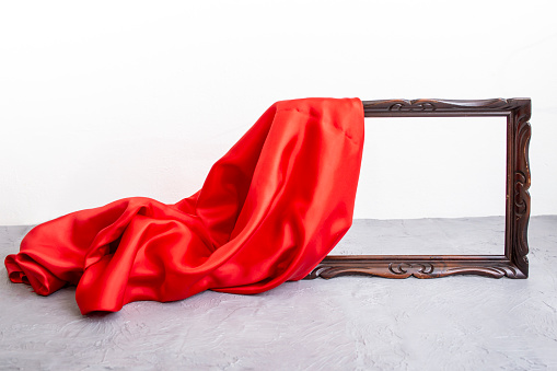 Red satin cloth unveiling a wooden brown frame, on cement table top and white background, mockup for presentation