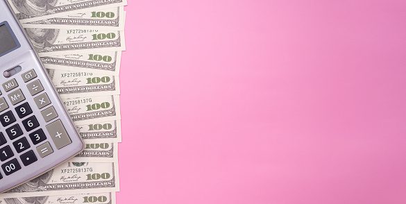 The flat lay of a calculator on US dollars banknote isolated a pink background. Space for text.