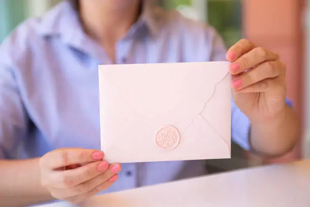 Closeup photography of woman,holding pink invitation envelope with wax seal.