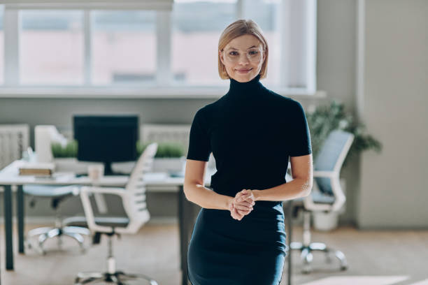 istock Confident businesswoman looking at camera and smiling while standing in the office 1472941086