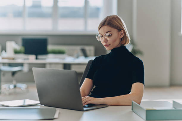 istock Confident young businesswoman using laptop while sitting at her working place in office 1472941137